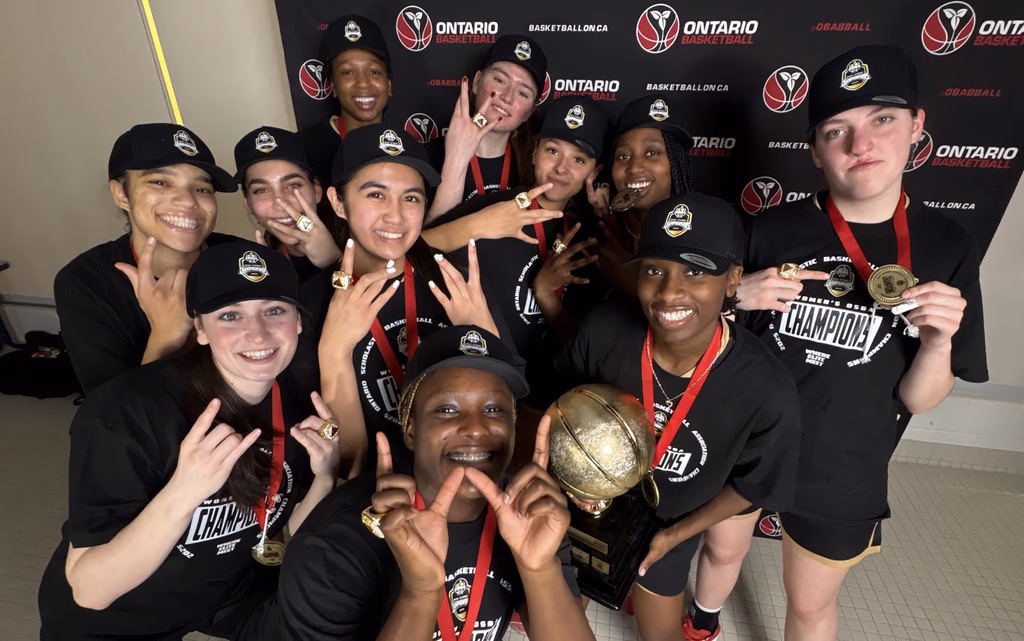 Capital Courts Academy players celebrate with medals, championship hats and t-shirts, and a gold basketball trophy, in front of an Ontario Basketball media backdrop.